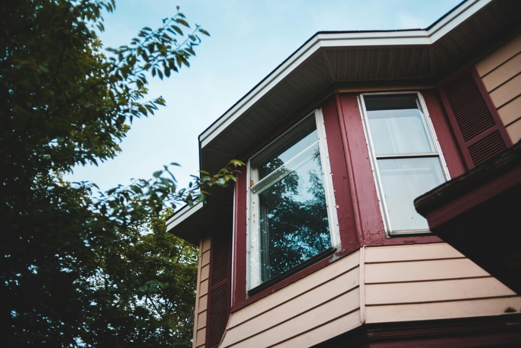 From below of cozy residential cottage with geometric facade and windows reflecting green trees and sky